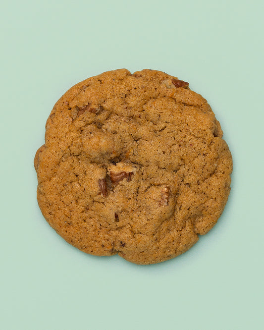 Close-up of the Pecan Sweet Potato Chai Cookie, showcasing its golden-brown exterior with hints of warm spices. The soft, chewy texture is packed with sweet potato, crunchy pecans, and aromatic chai flavors, creating the perfect balance of sweetness and spice. A decadent treat with cozy, fall-inspired flavors in every bite. 
